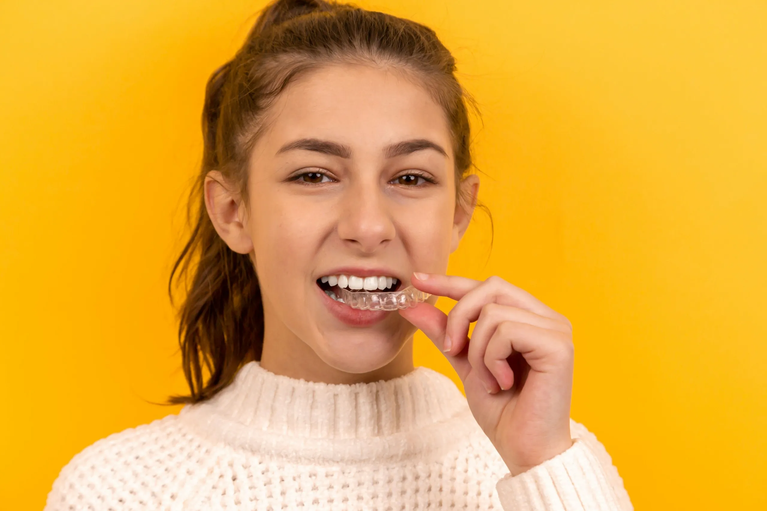 A smiling teenage girl putting in a clear aligner