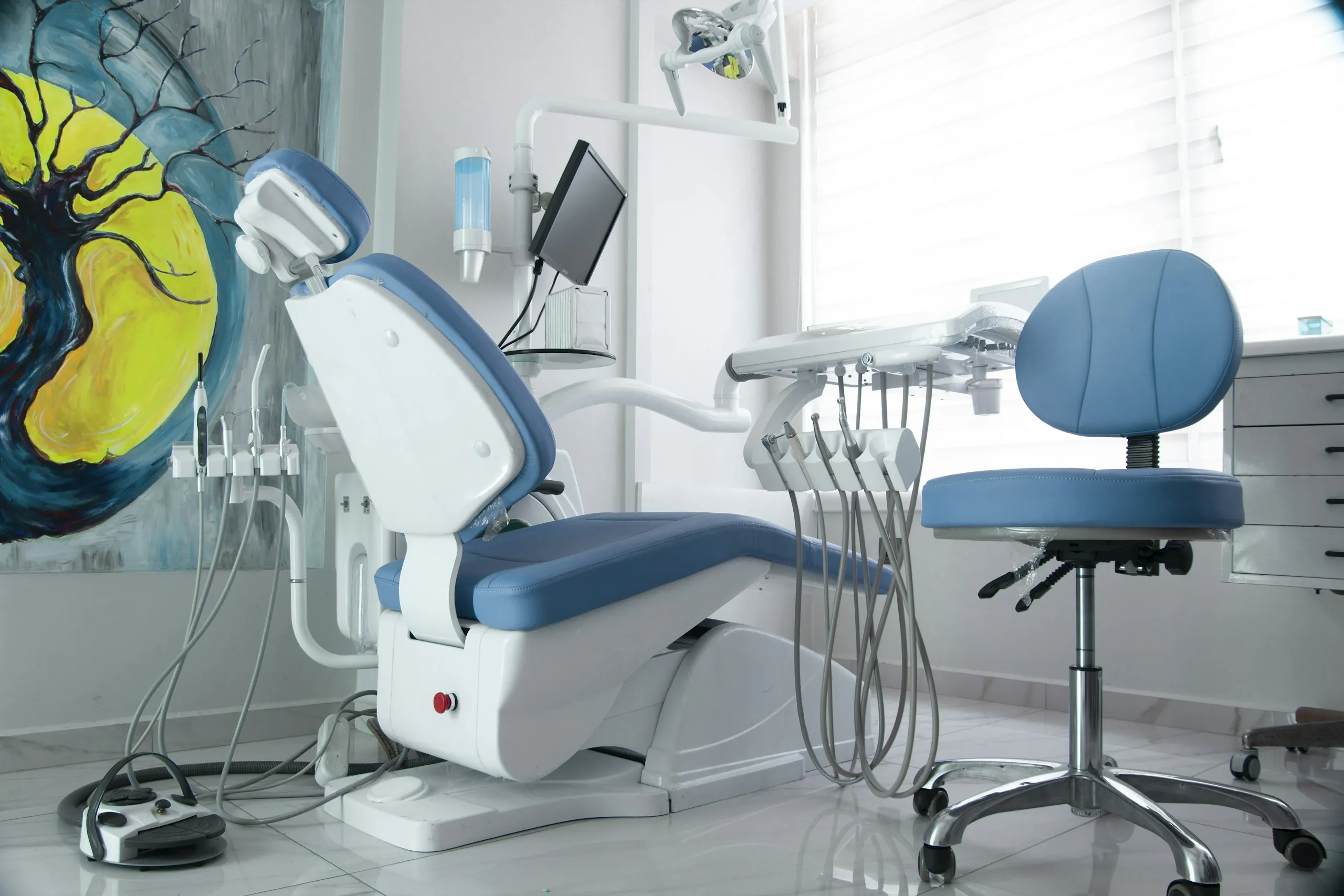 A blue treatment chair by a window under a colourful mural